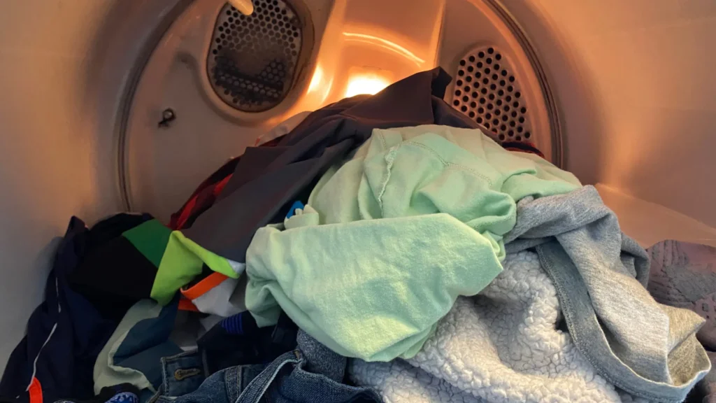 Clothes inside an open dryer drum with its interior light on