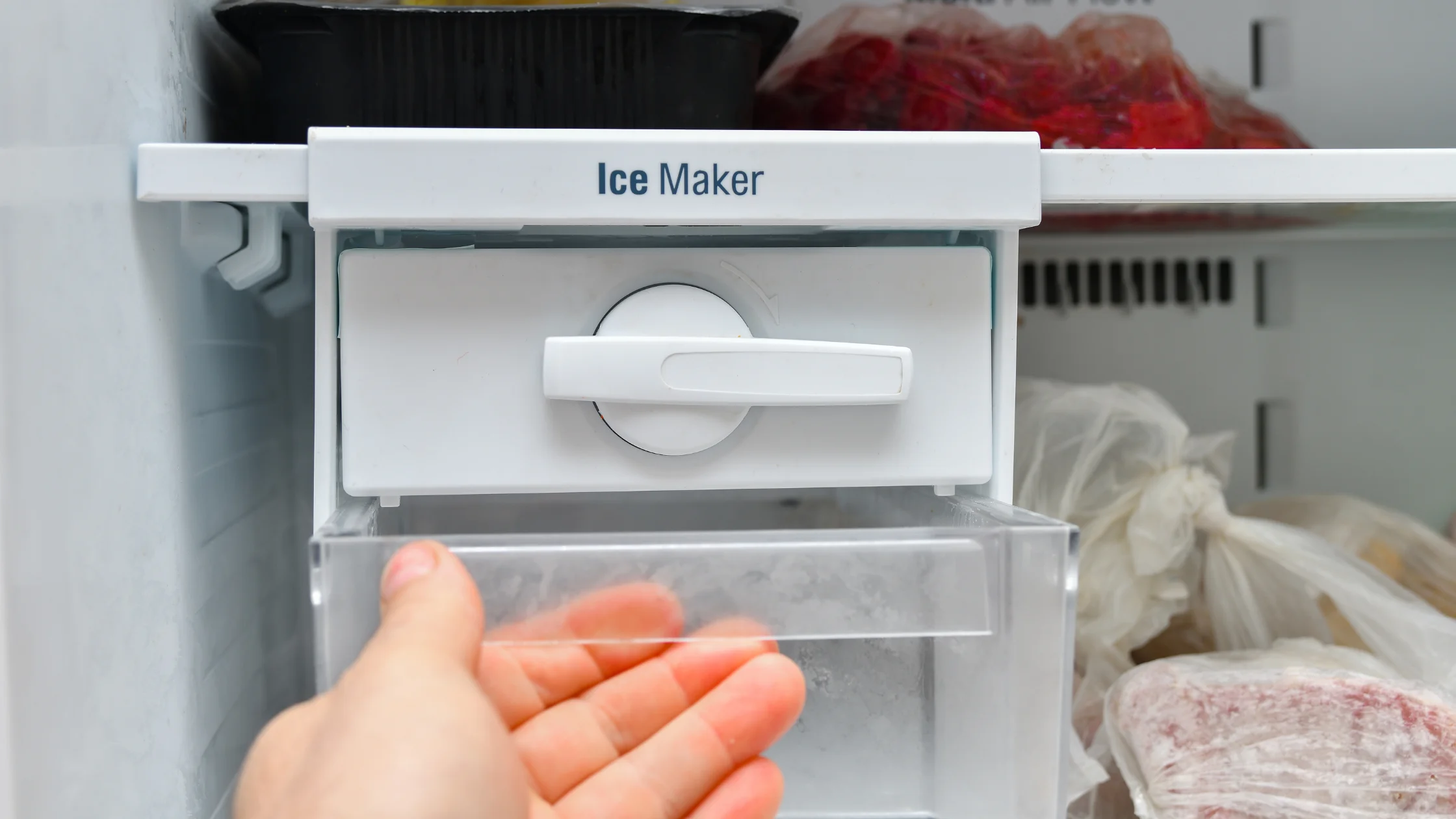 A hand holding the clear bin beneath a manual twist-tray ice maker